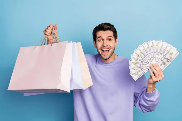 Photo of impressed young brunet guy hold bags money wear pullover jeans isolated on blue color background — Stockfoto