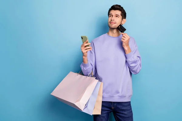 Photo of nice millennial brunet guy hold bags card telephone look up wear pullover isolated on blue color background — Foto de Stock