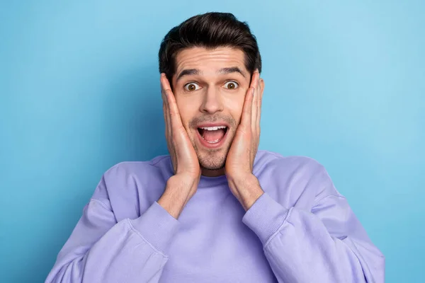 Photo of impressed young brunet guy hands face wear sweatshirt isolated on blue color background — Zdjęcie stockowe