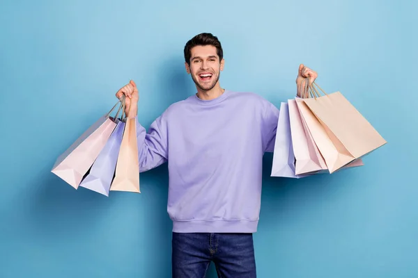 Photo of hooray young brunet guy hold bags wear sweater jeans isolated on blue color background — Stockfoto
