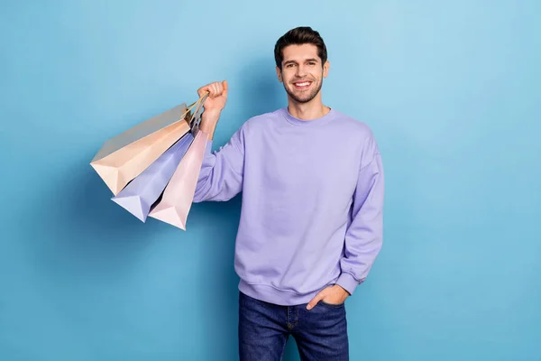 Porträtt av attraktiv glad kille som håller i handväskor nya saker isolerade över ljusblå färg bakgrund — Stockfoto