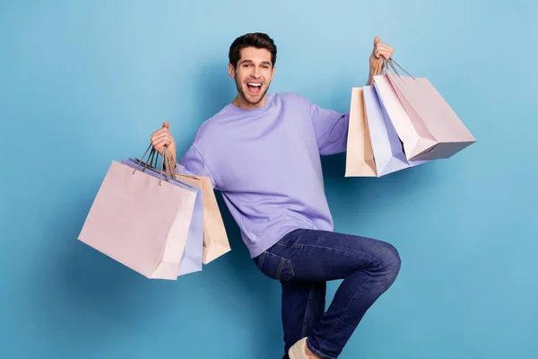 Photo of impressed millennial brunet guy hold bags yell wear sweater jeans isolated on blue color background — Foto de Stock