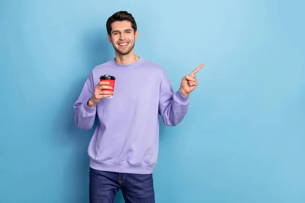 Portrait of attractive guy drinking tea showing copy space to go eco friendly cup isolated over bright blue color background — Stockfoto