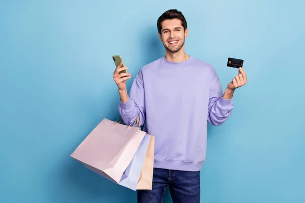 Foto van goede jonge brunet jongen hold bags kaart telefoon slijtage pullover jeans geïsoleerd op blauwe kleur achtergrond — Stockfoto