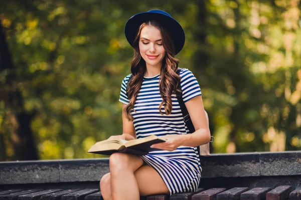 Photo of shiny charming young lady wear striped dress headwear rucksack smiling reading interesting story outdoors urban city park — Stock Fotó