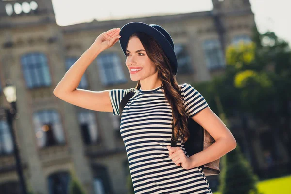 Photo of pretty charming young lady wear striped dress headwear rucksack smiling enjoying warm weather outdoors urban city park — Fotografia de Stock