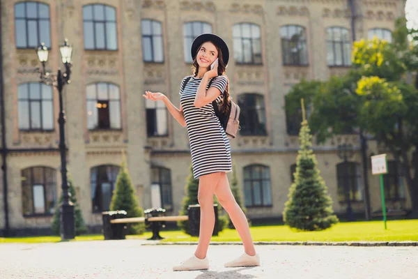 Foto de linda adorable joven mujer vestida a rayas gorra mochila caminando hablando dispositivo moderno sonriendo paisaje exterior —  Fotos de Stock