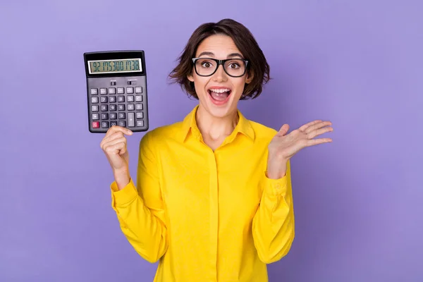 Zdjęcie prezesa młoda brunetka pani trzymać kalkulator krzyczeć nosić okulary żółta koszula izolowane na fioletowy kolor tła — Zdjęcie stockowe
