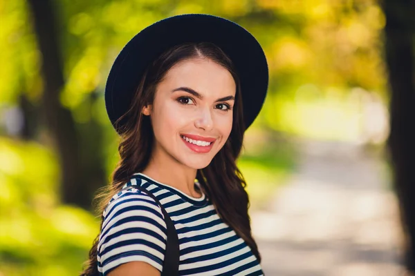 Φωτογραφία από αρκετά γλυκό νεαρή κοπέλα φορούν ριγέ φόρεμα καπέλο σακίδιο με χαμόγελο περπάτημα απολαμβάνοντας ζεστό καιρό σε εξωτερικούς χώρους αστικό πάρκο της πόλης — Φωτογραφία Αρχείου