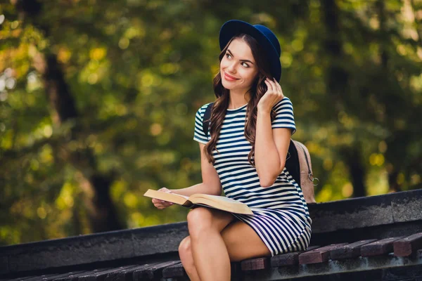 Photo of attractive sweet young woman dressed striped outfit cap backpack reading good book outside landscape — Stock Fotó