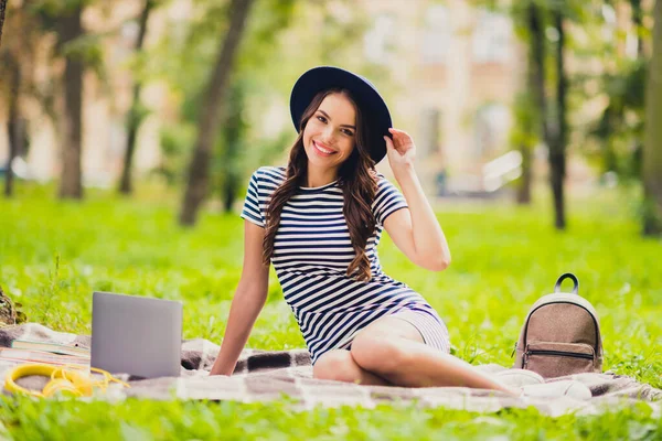 Portrait of beautiful cheerful girl doing home task work project sitting on cover watching video touching cap on fresh air outdoors — Fotografia de Stock