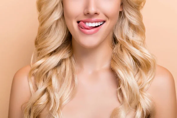 Retrato de vista recortada de atractiva chica alegre de pelo ondulado lamiendo labio fresco aliento chapas aisladas sobre fondo de color pastel beige — Foto de Stock
