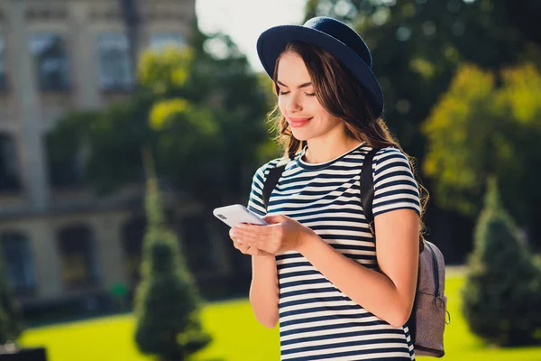 귀엽고 귀여운 젊은 여성의 사진 줄무늬 캡백 을 착용하고 현대 장비 메시지를 쓰고 풍경 밖에서 미소짓는 모습 — 스톡 사진