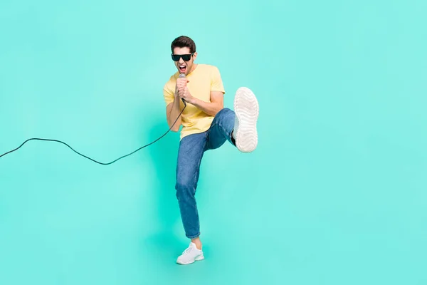 Full body photo of crazy brunet millennial guy sing wear glasses t-shirt jeans shoes isolated on teal background — стоковое фото