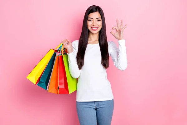 Foto de cool millennial morena dama mantenga bolsas muestran okey desgaste simple tela aislada sobre fondo de color rosa —  Fotos de Stock