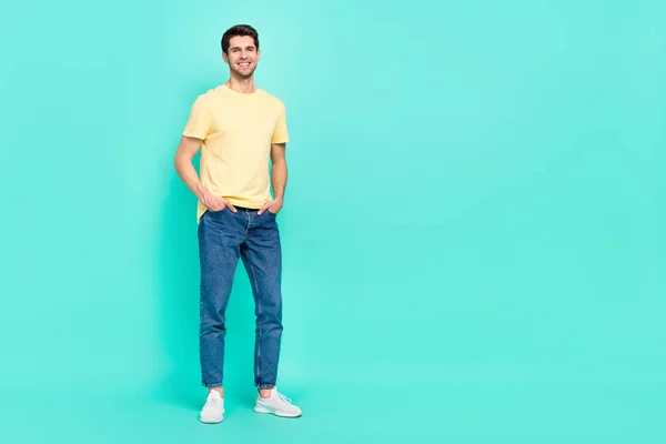 Full size photo of cute brunet young guy near empty space wear t-shirt jeans shoes isolated on turquoise color background — Foto de Stock