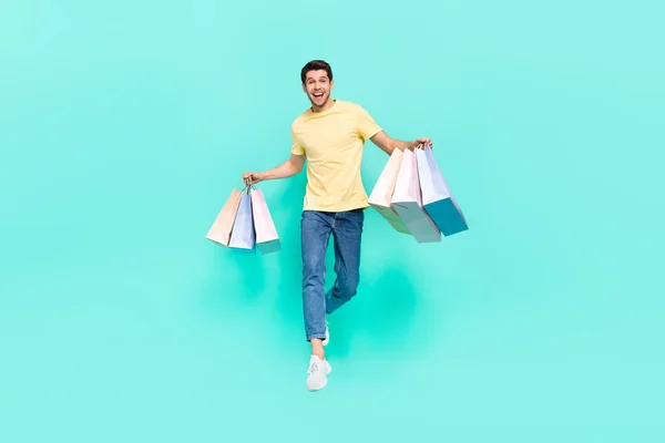 Full size photo of nice brunet guy run with bag wear t-shirt jeans shoes isolated on teal background — Foto de Stock