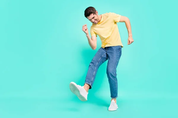 Полная фотография оптимистичной брюнетки молодой парень танцы носить футболки джинсы кроссовки изолированы на бирюзовом фоне — стоковое фото
