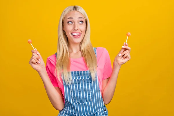 Retrato de chica linda alegre atractiva comiendo caramelos que se divierten lamiendo el labio aislado sobre fondo de color amarillo brillante — Foto de Stock