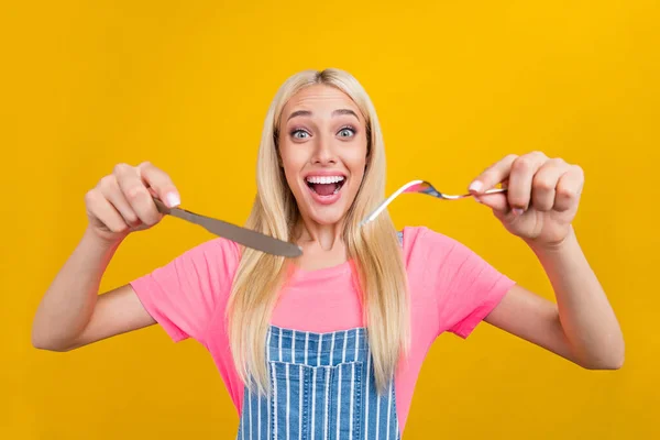 Portrait of attractive cheerful blond girl holding fork knife eating cfresj mealuisine isolated over bright yellow color background — стоковое фото