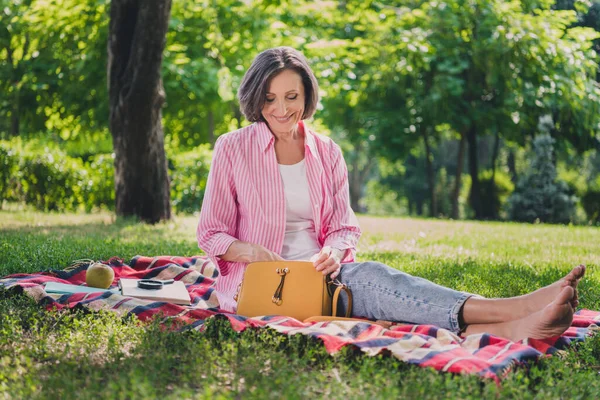 Photo of attractive shiny lady pensioner wear pink shirt sitting blanket looking inside open bag outdoors countryside garden — Fotografia de Stock