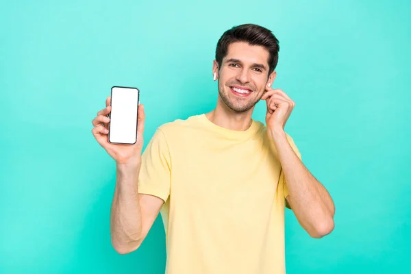 Фото крутої брюнетки тисячолітній хлопець показує телефонні навушники з футболкою ізольовані на кольоровому фоні — стокове фото