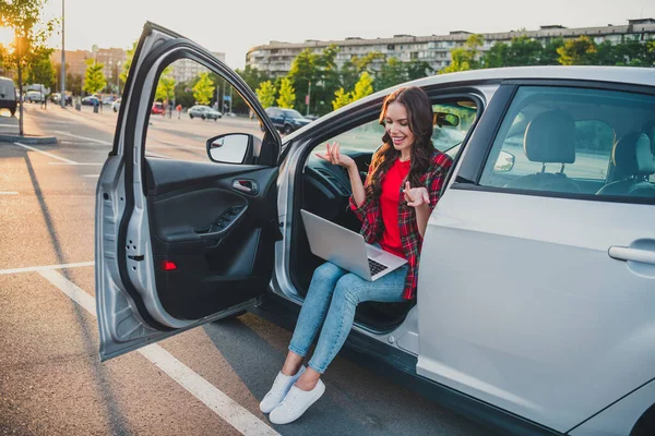 Retrato de chica atractiva de pelo ondulado alegre sentada en auto haciendo videollamada comunicándose en el estacionamiento al aire libre —  Fotos de Stock