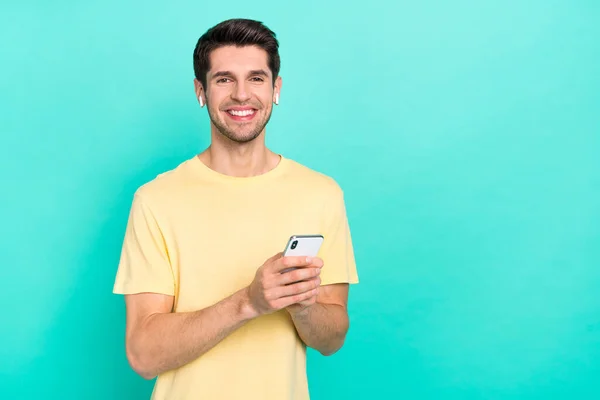 Photo of cute brunet millennial guy hold telephone wear t-shirt headphones isolated on teal color background — Fotografia de Stock