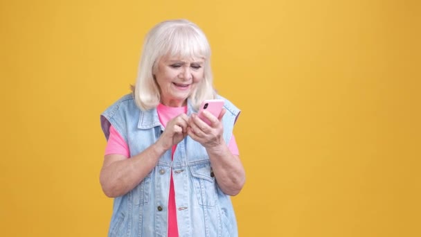 Η ηλικιωμένη κυρία χρησιμοποιεί τη συσκευή ανάγνωσης εφαρμογών μετά από απομονωμένο ζωηρό χρώμα φόντου — Αρχείο Βίντεο