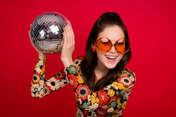 Foto av upphetsad vacker kvinna bära blomma tryck klänning glasögon håller disco boll isolerad röd färg bakgrund — Stockfoto