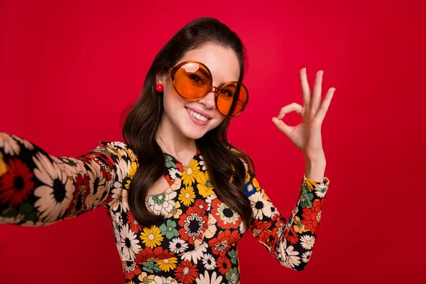 Photo of cute sweet young lady dressed flower print outfit glasses recording video showing okey sign isolated red color background — Stockfoto