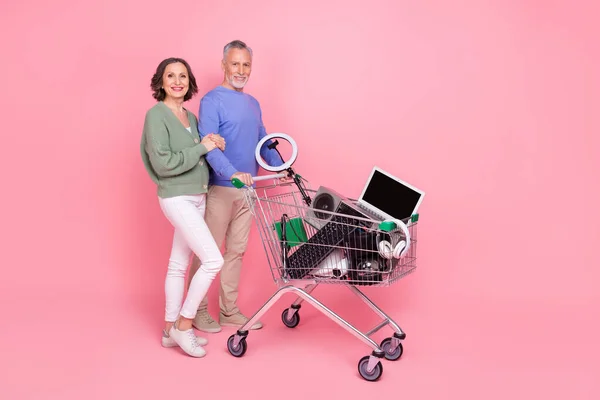 Full size photo of two positive friendly partners hold hand push trolley isolated on pink color background — стоковое фото