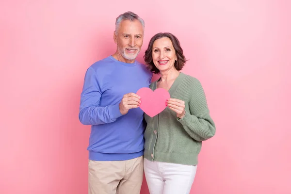 Portrait of two attractive cheerful people embracing holding heart sign isolated over pink pastel color background —  Fotos de Stock