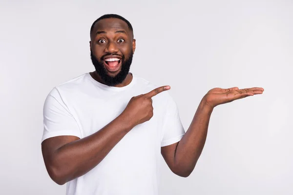 Photo of excited funky guy dressed casual t-shirt holding arm pointing empty space isolated white color background — Stok fotoğraf