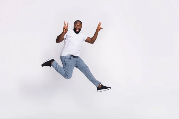 Photo of pretty cute guy dressed casual t-shirt jumping high running v-sign empty space isolated white color background — Stockfoto