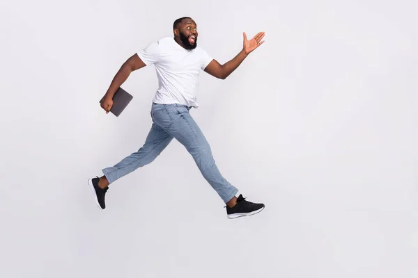 Photo of excited funky guy dressed casual t-shirt jumping high holding modern gadget empty space isolated white color background — ストック写真