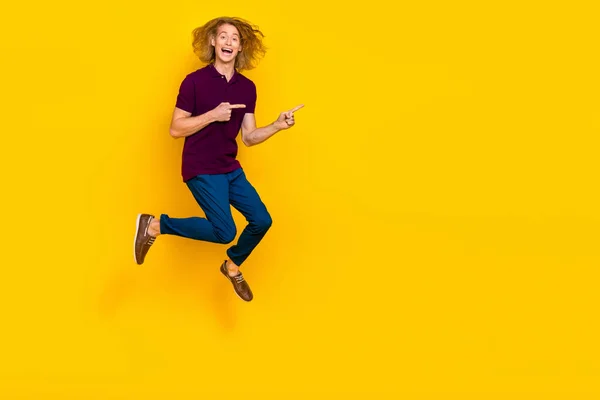 Full size photo of overjoyed energetic man jumping direct fingers empty space isolated on yellow color background — Stok fotoğraf