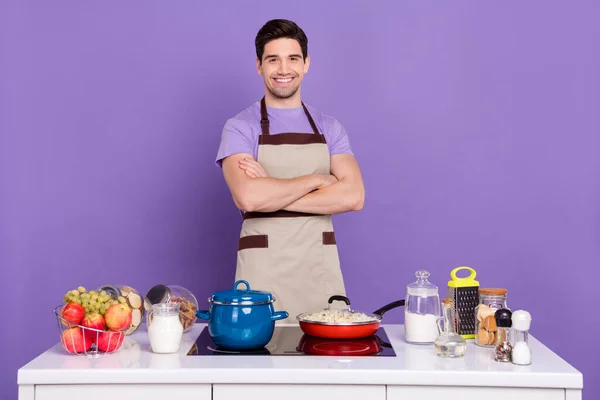 Foto de cara bastante confiante usar cinza avental braços cruzados pronto cozinhar prato saboroso isolado cor violeta fundo — Fotografia de Stock