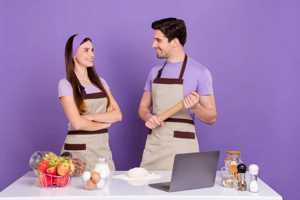 Foto de alegre novio positivo novia vestidos trajes de chef listo hornear galletas gadget aislado color púrpura fondo — Foto de Stock