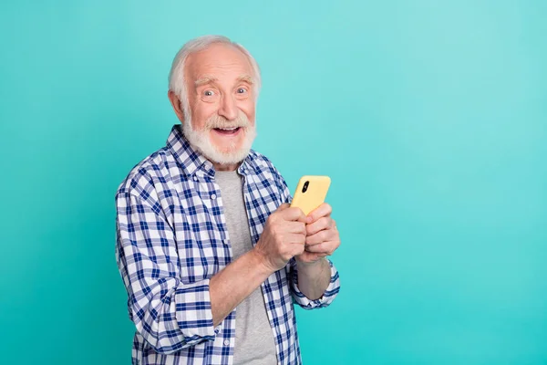 Photo of smiling pensioner using smartphone to chat with his friends isolated on turquoise color background — Photo