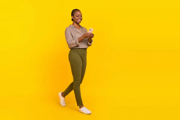Photo of cheerful positive lady dressed checkered shirt earphones walking empty space isolated yellow color background — Stock Fotó