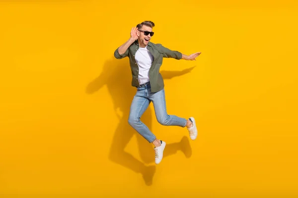 Pełna długość ciała rozmiar widok atrakcyjny wesoły ciekawski facet skoki słuchanie odizolowane na jasnożółtym tle kolor — Zdjęcie stockowe