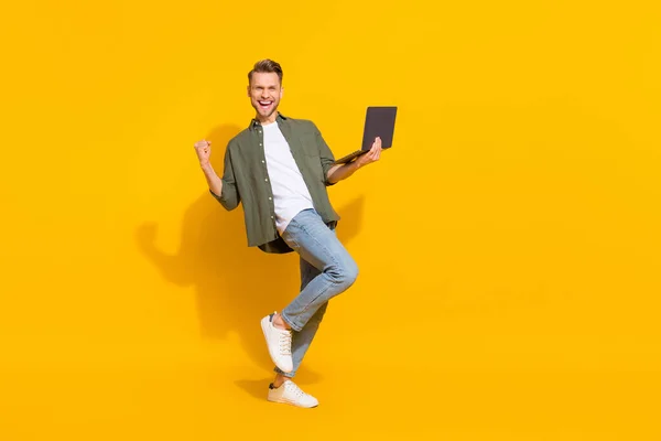 Повнорозмірний вигляд тіла привабливого веселого хлопця, який використовує ноутбук, радіючи веселому ізольованому на яскраво-жовтому кольоровому фоні — стокове фото