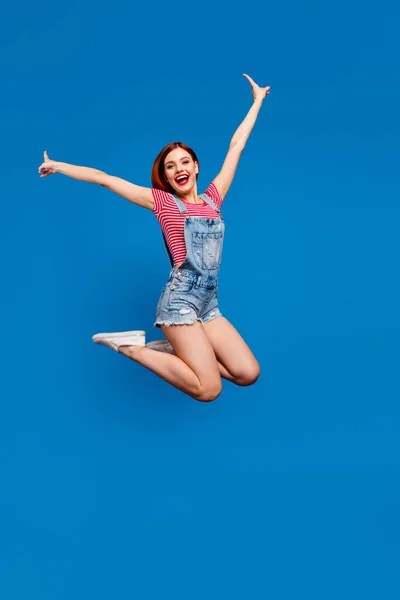 Vertical photo of funky excited young lady dressed denim clothes jumping high rising arms hands isolated blue color background — Stock Photo, Image