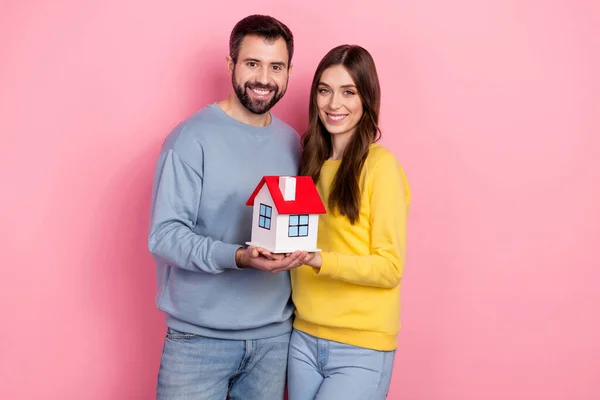 Φωτογραφία από δύο θετικά ικανοποιημένους εταίρους κατέχουν αποδεικνύουν μικρό σπίτι απομονωμένο σε ροζ φόντο χρώμα — Φωτογραφία Αρχείου