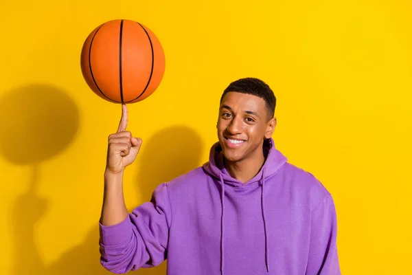 Portrait of attractive cheerful sportive guy spinning on forefinger orange ball isolated over bright yellow color background — 스톡 사진