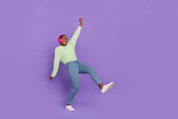 Full length photo of overjoyed energetic dancing female in green pullover listen music in headset isolated on violet color background — ストック写真