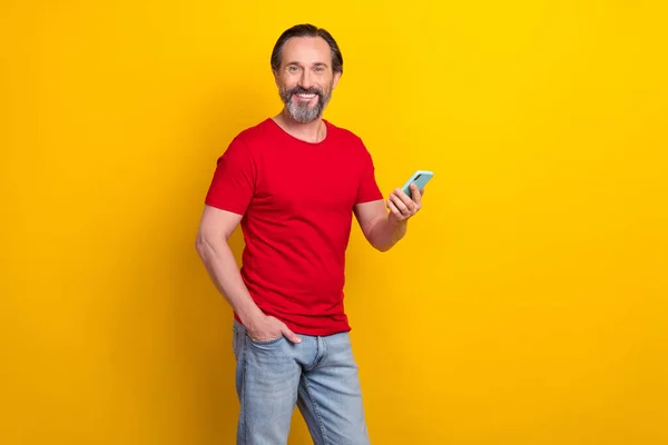 Foto van goede jonge brunet man houden telefoon dragen rood t-shirt geïsoleerd op gele kleur achtergrond — Stockfoto