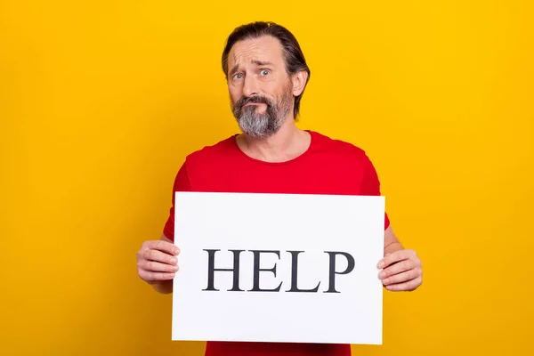 Photo of unhappy upset guy pensioner dressed red t-shirt holding help board isolated yellow color background — Foto de Stock