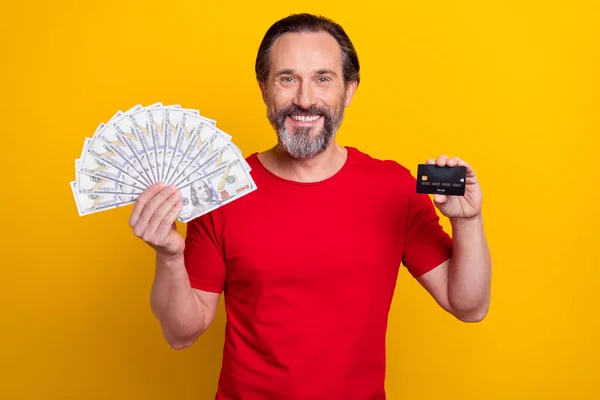 Photo of pretty funny guy pensioner dressed red t-shirt showing money fan credit card isolated yellow color background — Photo